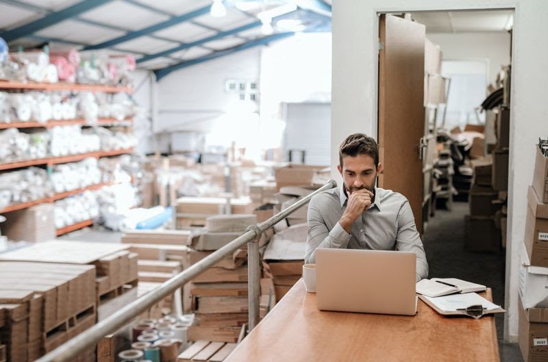 business accounting and management - man working on a laptop inside a warehouse