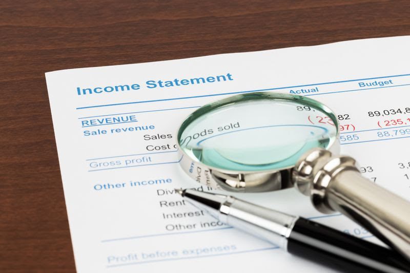 income statement with a magnifying glass and a pen on top of it
