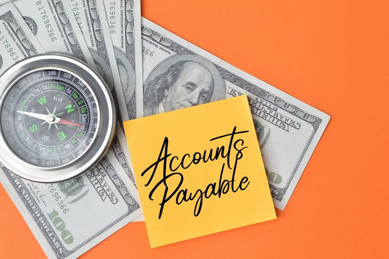 accounts payable specialist - Two hundred-dollar bills, a compass, and an orange post-it note with “accounts payable” written in cursive.