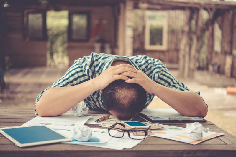 bookkeeping services - A guy holding his head down a table with scattered paper