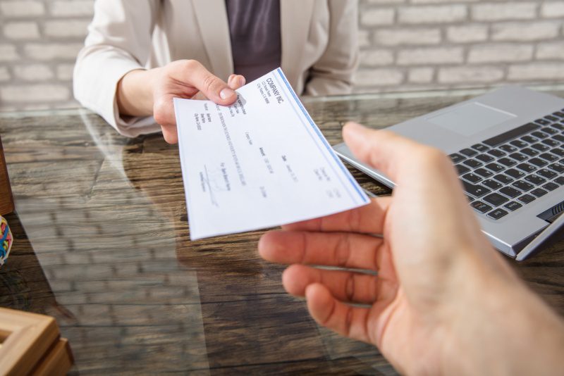 shot of an employer handing a payroll cheque to their employee